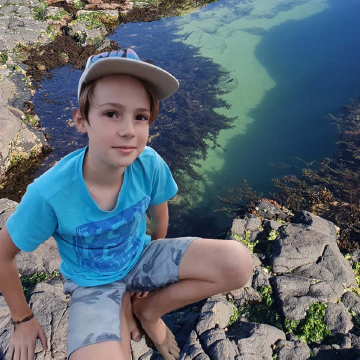 Young person sitting by rocks and water looks up at camera