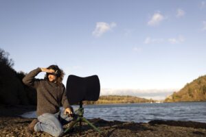 Person looking left in landscape with body of water and mountains.
