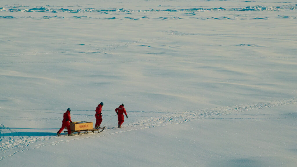 Three people pull a sled on ice