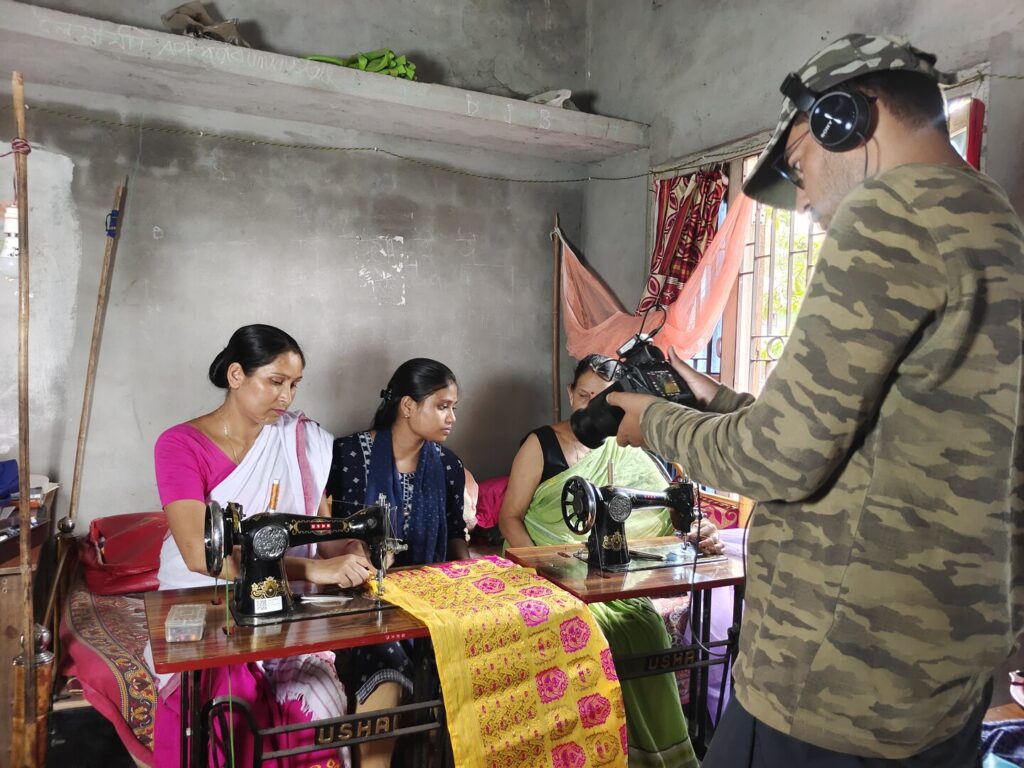 People sitting at sewing machines and person with camera