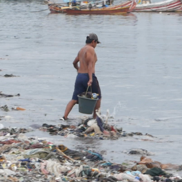 Person looks at water surrounded by trash