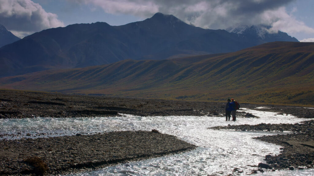 Two people standing in water with mountains behind.