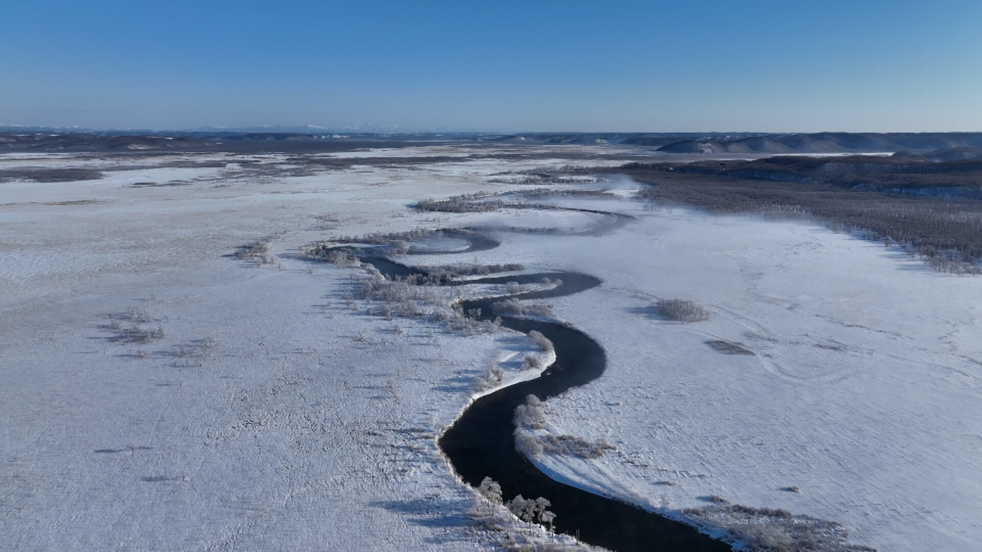 img-672fc1232cfc3 Wide shot of wintery landscape with body of water in center.