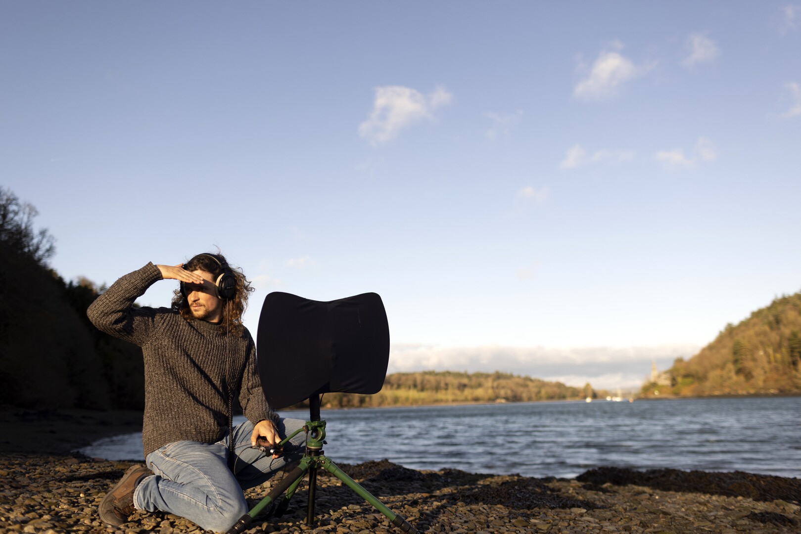 Person looking left in landscape with body of water and mountains.