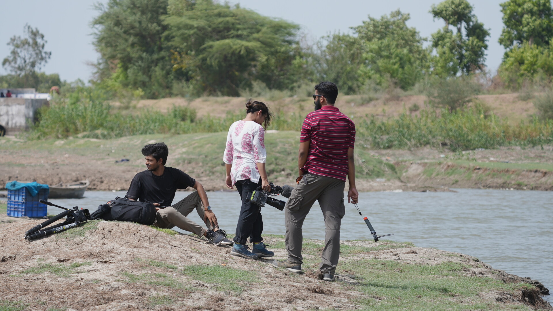 Three people stand by water with filmmaking gear.