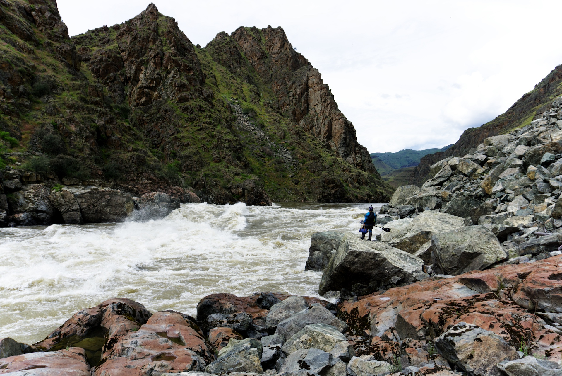 Person standing next to rapids in mountainous landscape.