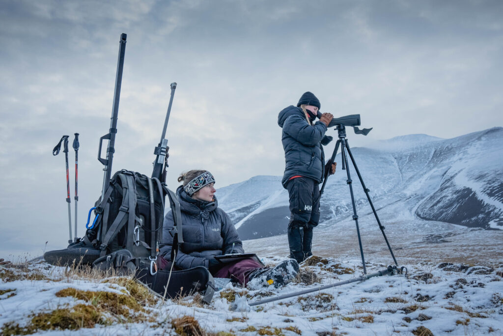 Two people with gear stand on wintery landscape.
