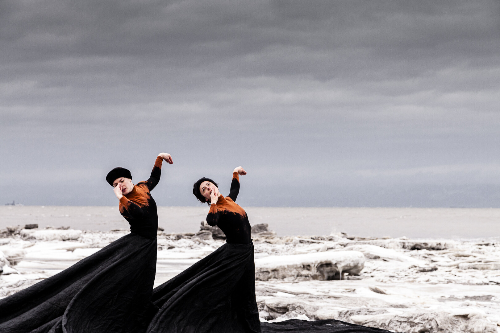 Two dancers in black with orange dresses moving outside.