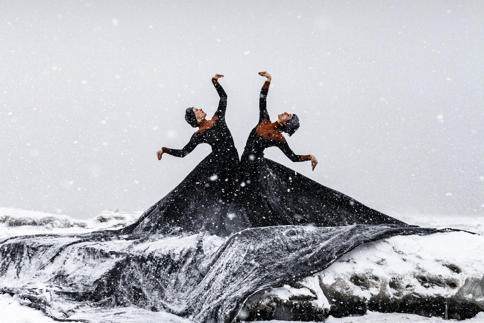 Two dancers in black with orange dresses moving outside.