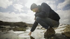 Person crouches and puts hand in water.