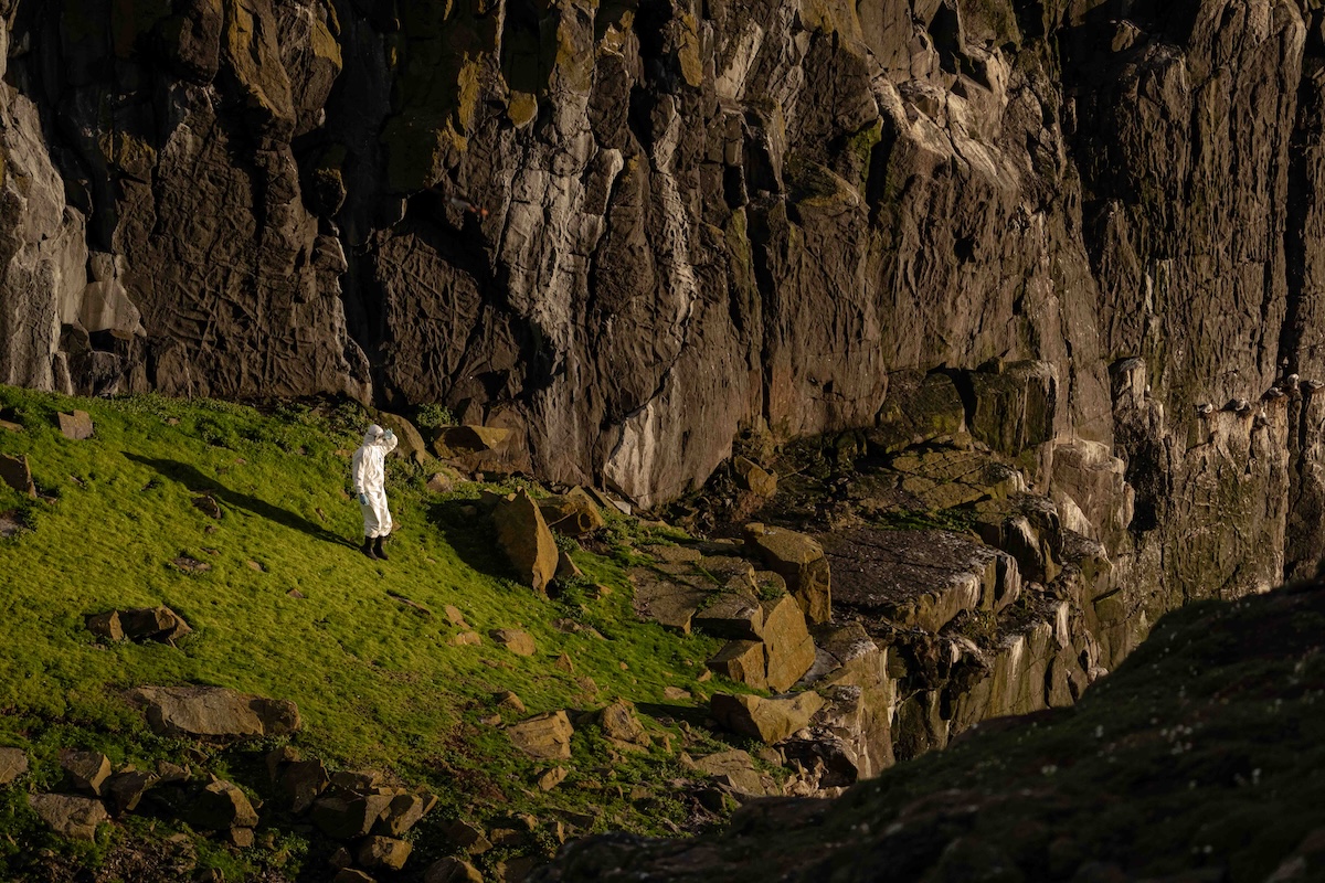 Person in protective gear stands in rocky environment.