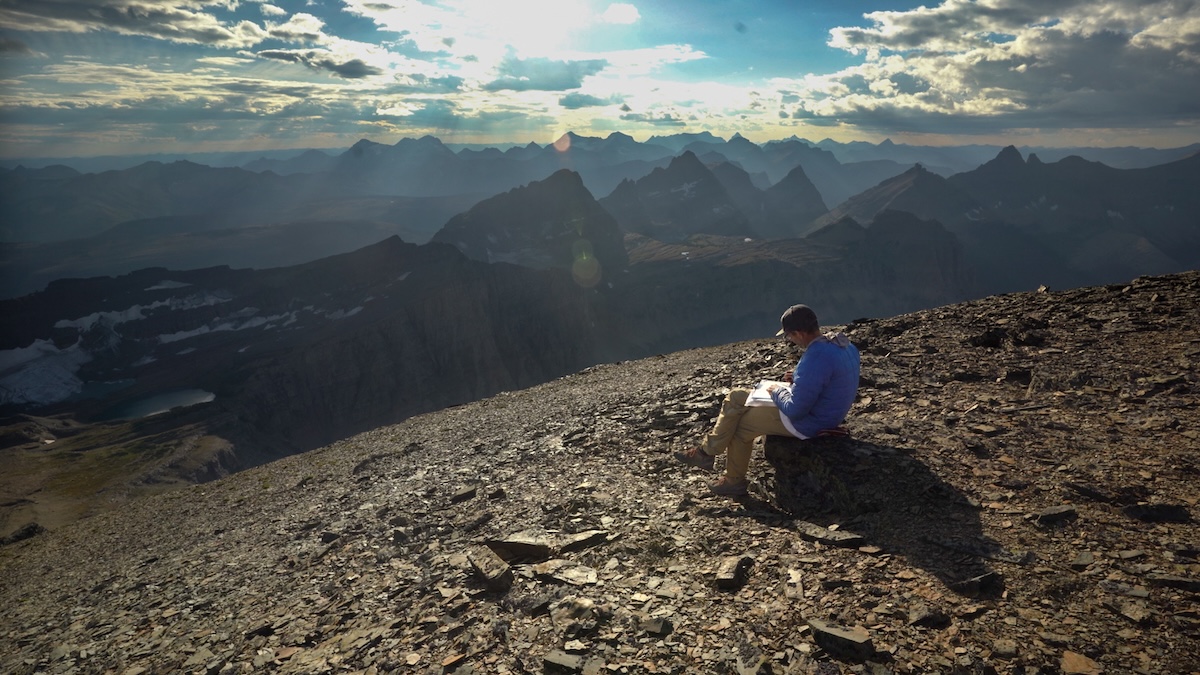 Person sitting in mountains and drawing.