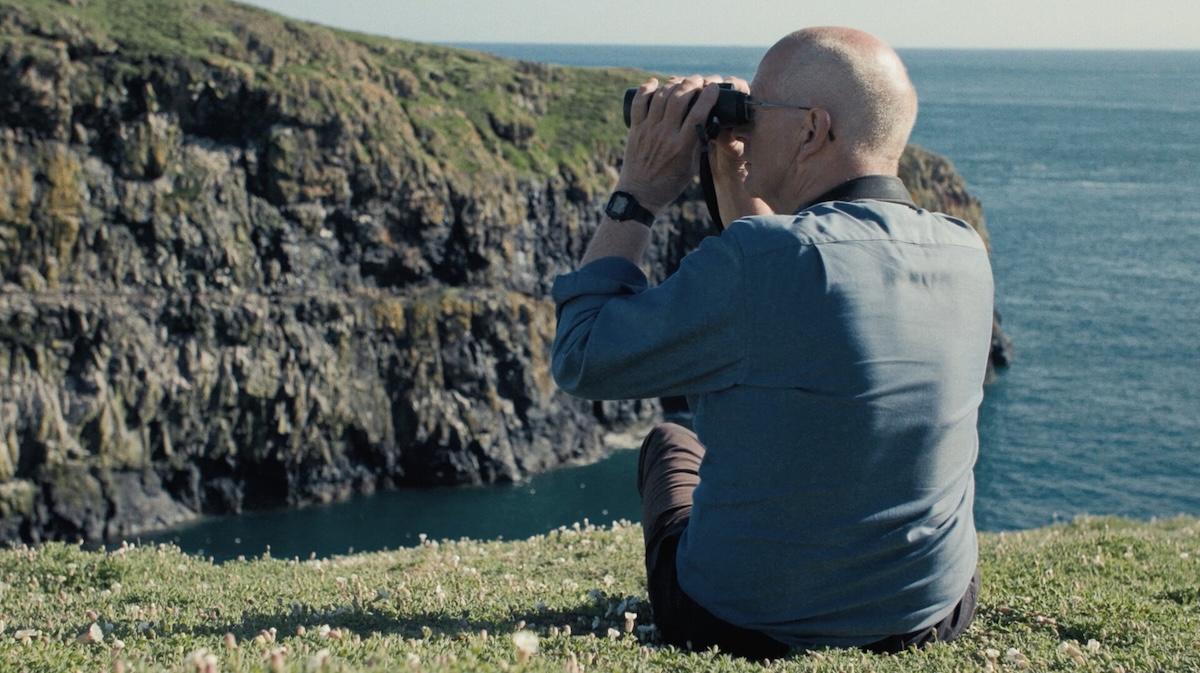 Person sitting on cliff with binoculars.